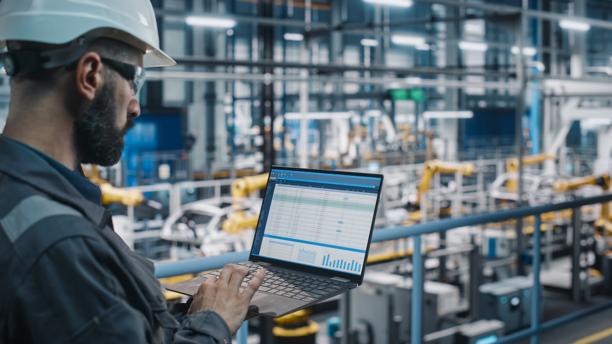 Factory Engineer in Work Uniform Using Laptop Computer with Spreadsheet Software. Working with Software at Automotive Industrial Manufacturing Facility Dedicated for Vehicle Production to represent manufacturer rep industry